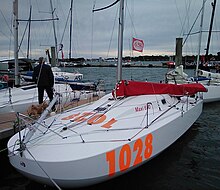 Bateau blanc à l'avant très large et très arrondi, amarré au ponton. Il porte en rouge le numéro 1028.