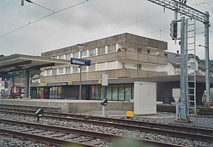 Single-story flat-roofed building with block overhead, tracks in the foreground