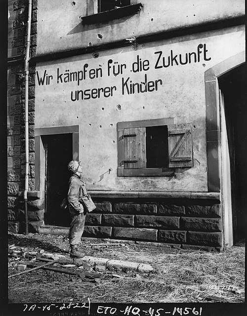 PFC Abraham Green, medic, New Haven, Conn., 253rd Regiment, 63rd Division, reads a German propaganda slogan, "We fight for the future of our children"