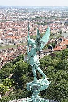 Statue de l'archange Michel frappant le dragon ; en arrière-plan, le sud de l'agglomération lyonnaise