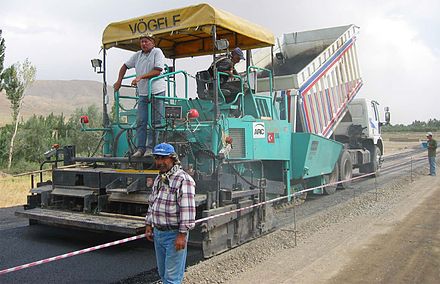 A machine laying asphalt concrete, fed from a dump truck