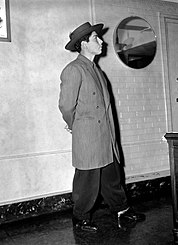 Frank H. Tellez, a Pachuco youth, wears a zoot suit while arrested in the Zoot Suit Riots. Pachucos were the first to reclaim the word Chicano as a form of pride. A man arrested during the Zoot Suit Riots models a zoot suit and pancake hat in a Los Angeles County jail on June 9, 1943.jpg