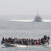 Embarcación sobrecargada de inmmigrantes irregulares, junto a un guardacostas español.