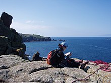 Climber consulting a 'physical' climbing guidebook at the top of a route at Sennen Cove Climber reading guidebook.jpg