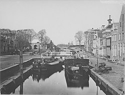 Het Damsterdiep in 1874 met links op de achtergrond de Steentilpoort en het poortershuisje. Links op de voorgrond een rolpaal. Rechts een volgeladen turfschip.