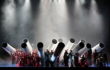 Photographie montrant une troupe de comédiens et chanteurs sur scène.