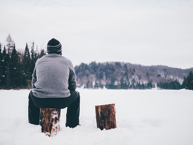 File:Man sits on log in snow (Unsplash).jpg