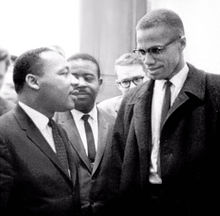 Malcolm X and Martin Luther King speak to each other thoughtfully as others look on