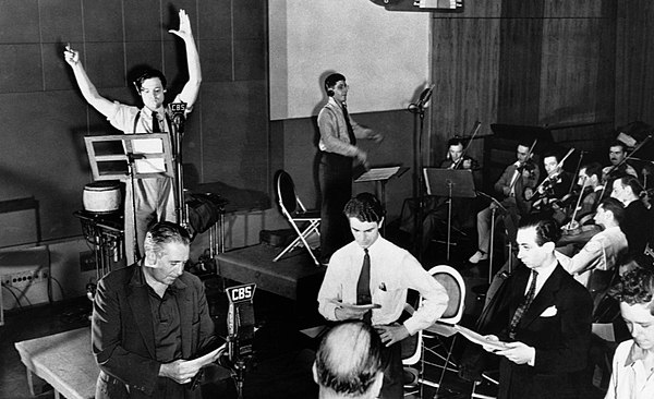 Orson Welles, arms upraised, directs a rehearsal of CBS Radio's The Mercury Theatre on the Air. Bernard Hermann conducts the CBS Radio orchestra; acto