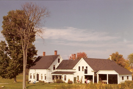 Connected farm in Windham, Maine. The barn dates from the late 18th century. The house was built in three stages during the 19th century. The unconnected garage was a 20th-century addition. All doors of the structure are visible in this view from the south side, where winter sun would melt accumulated snow and ice. Following the 20th-century outbreak of Dutch elm disease only one American elm remains of the line which provided summer shade along the southern and western sides of the building. NewEnglandConnectingFarm.png