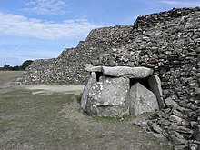 Énormes dalles debout côte à côte formant un polygone, et supportant une grande table. En fond, l'arrière du cairn secondaire, vu en coupe dans la zone dévastée, forme un escalier à trois marches.