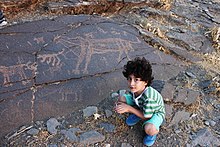 Curious boy sitting near petroglyphs Taimerh 3.jpg