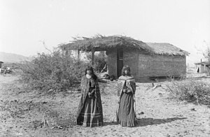 Two Mojave girls standing in front of a small dwelling with a thatched roof, 1900 Two Mojave Indians girls standing in front of a small dwelling with a thatched roof, 1900 (CHS-1241).jpg