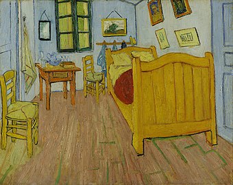 A small room with paintings on the wall, two chairs, a single bed and a table