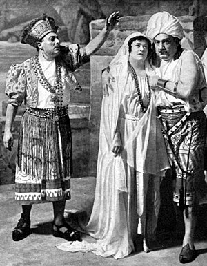 Three figures in exotic costumes; to the right a man and a woman embrace, while on the left another man addresses them, left arm raised perhaps in a gesture of blessing