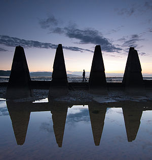 Cramond causeway pylons in Edinburgh in the evening light with a walker strolling along the causeway.