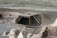 A reconstruction of a pit-house at the Step House ruins in Mesa Verde National Park, United States, shows the pit dug below grade, four supporting posts, roof structure as layers of wood and mud, and the entry through the roof. Pithouse at Step House Mesa Verde 1.jpg