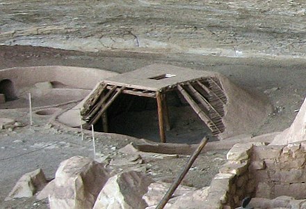 A reconstruction of a pit-house at the Step House ruins in Mesa Verde National Park, United States, shows the pit dug below grade, four supporting posts, roof structure as layers of wood and mud, and the entry through the roof.