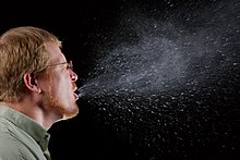 man sneezing, with droplets dispersing widely into the surrounding air