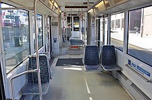 El interior de un tranvía, que muestra dos ventanas grandes, agarraderas, botones y una pequeña escalera que conduce a una sección superior con asientos orientados hacia adelante y hacia atrás.