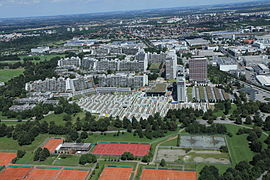 Vue aérienne du village olympique. À l'avant-plan, des courts de tennis, puis le quartier des bungalows, puis les grandes tours des hommes, et enfin en arrière-plan le reste de la ville.