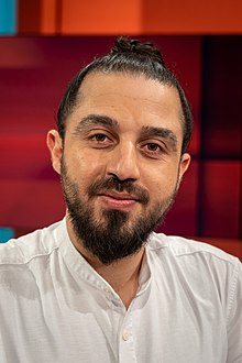 Porträt des Menschenrechtsaktivisten Tareq Alaows vor roter Kulisse