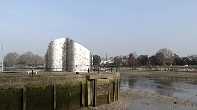 Bulky shining sculpture or landmark, Liquidity erected 2002 at the apex Ferry Wharf, Brentford, marking a then-dry entrance to the Grand Union Canal from the River Thames's Tideway as at low tide.