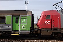 Une locomotive grise et rouge tire un wagon de passager en aluminium.