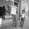 Israël. Kirjat Gat (Kiryat Gat). Man verbergt gezicht achter Franstalige krant L'Information d'Israël, naast hem een ijsetende jongen met zonneklep (255-3084).jpg