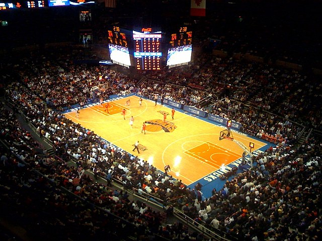 The inside of an arena with large scoreboard visible, which is set up for basketball.