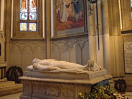 Inside a gothic chapel, a marble effigy of a bearded emperor in uniform lies atop an intricately carved stone sarcophagus