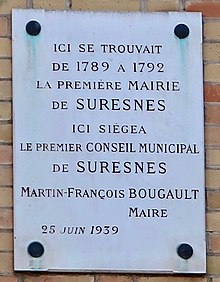 Photographie en couleur d'une plaque posée verticalement sur la façade d'un bâtiment.