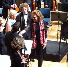 photographie en couleurs, la compositrice serre la main du premier violon dans l'orchestre