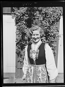 Black-and-white image of Norwegian woman Aslaug Huseklepp, standing with a vested dress in front of a tree, smiling at the camera