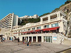 Le boulevard Prince de Galles sur la digue bordant la plage de la Côte des Basques à Biarritz. Au-dessus des douches pour baigneurs, se tient la terrasse du « bar de la Côte des Basque-Biarritz en bord de mer ». Ce bar-restaurant est la propriété des anciens rugbymans Marc Lièvremont et son frère Thomas.