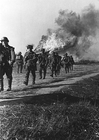 German soldiers march by a burning home in Soviet Ukraine, October 1941.
