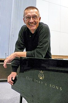 Emil Viklický apoyado en un piano Steinway y sonriendo a la cámara