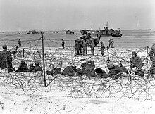 Prisioneiros alemães sentados na praia em um cercado de arame farpado após os americanos conquistarem a região.