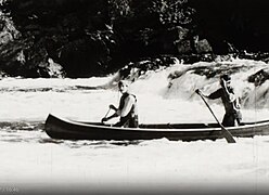 Grey Owl paddling in the bow of a canoe on the Mississagi River.