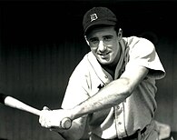 A baseball player smiles for the: camera while posing with a bat.