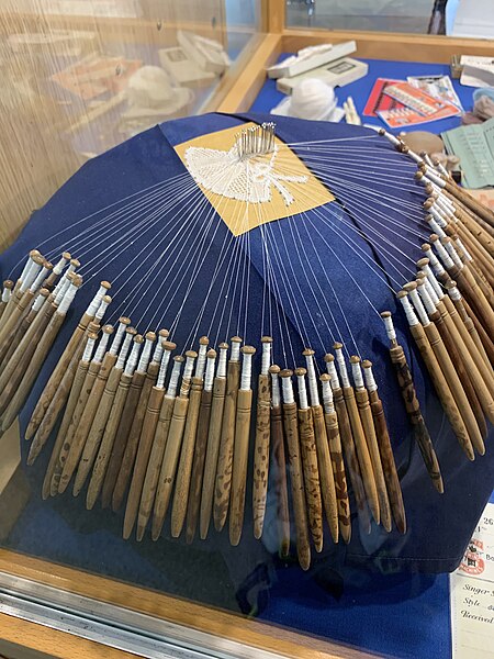 This shows lace bobbins on a lace making pillow on display at the Allhallows Museum in Honiton, England.
