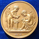 Rückseite der Medaille: Amor l. und Hymenaios r. sitzend, r. am Rand die brennende Fackel des Hymenaios (Quelle: Wikimedia)