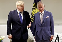 Charles standing next to Boris Johnson with the flag of the Commonwealth of Nations behind them