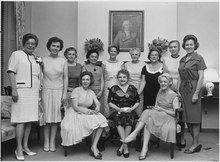 Een groepsfoto van 12 vrouwen, drie zittend en negen staand, gekleed in zakelijke jurken