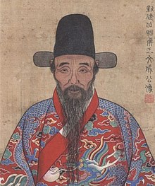 Kresba staršího muže s dlouhou černou bradkou, knírem a černou čepicí, který je oblečen do bohatě zdobeného červeno-modrého oděvu s límcem.