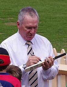 A white-skinned man signing on a cricket bat.