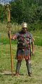 Aquilifer uit de tijd van de Gallische oorlog met signum.  De officier is uitgerust met een lorica hamata, gedragen op een Griekse linothorax, een Coolus-helm, gladius hispaniensis, kanen en laarzen geschikt voor koude streken.