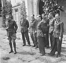 Foto dari enam laki-laki berpakaian seragam militer berdiri di hadapan pintu masuk ke sebuah bangunan