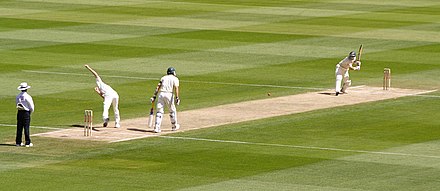 A bowler delivers the ball to a batsman during a game of cricket.