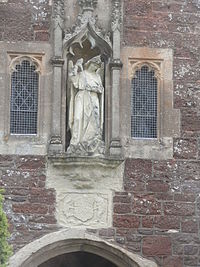 Porch, Church of St Michael and All Angels, with statue of St Michael the Archangel slaying a dragon. Below are displayed the armorials of the Courtenay family, Earls of Devon, sometime lords of the manor, worn away with only the supporters of a boar (dexter)and dolphin (sinister) still visible StMichaelPorchAlphingtonChurchDevon.jpg